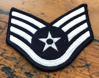 May include: A dark blue fabric patch with three white stripes and a white five-pointed star with a white circle in the center.