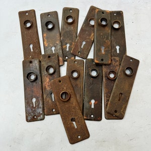 May include: A collection of vintage, antique, brass, metal, door, or cabinet, keyhole covers. The keyhole covers are in various shapes and sizes, and have a worn, aged, patina finish.