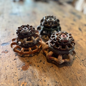 Könnte beinhalten: Nahaufnahme von drei antiken Metallventilen in Rost-, Orange- und Grüntönen. Jedes Ventil hat eine kreisförmige, sternförmige Oberseite. Sie liegen auf einer verwitterten Holzoberfläche.