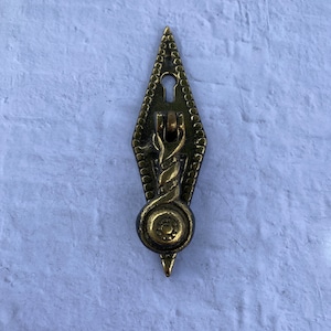 May include: A brass cabinet pull with a diamond-shaped design and a keyhole. The pull has a decorative, twisted, rope-like handle with a round knob at the bottom.