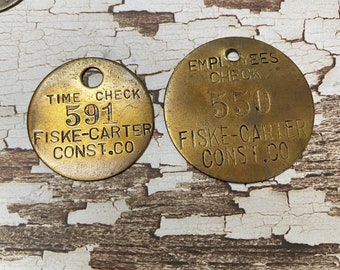 May include: Two round brass tokens with black lettering. The top token reads "Employees Check 550 Fiske-Carter Const. Co.". The bottom token reads "Time Check 591 Fiske-Carter Const. Co."