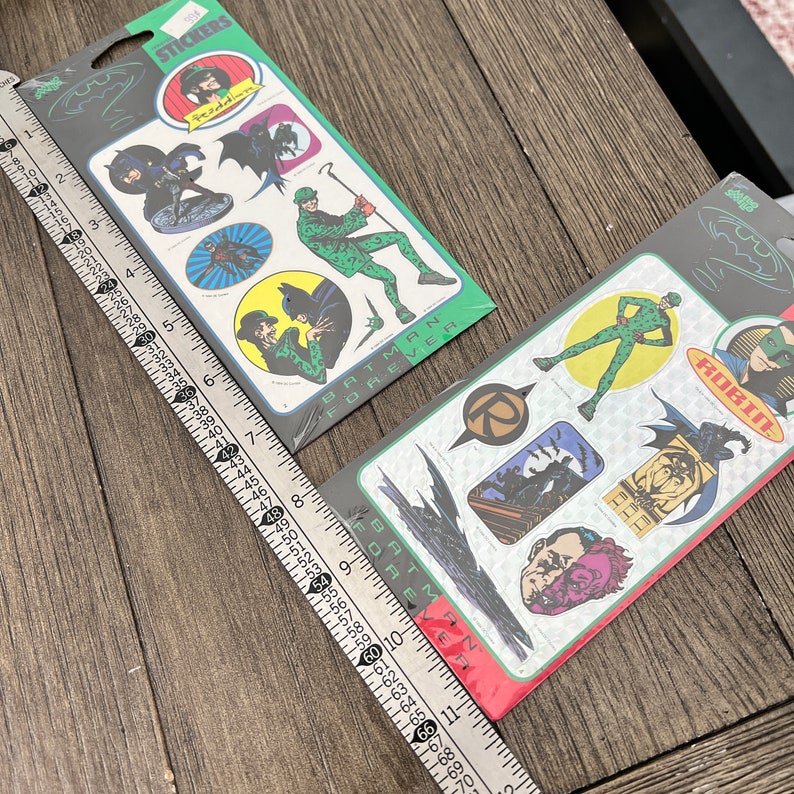 Peut inclure: Deux paquets d'autocollants Batman Forever. Le premier paquet pr&eacute;sente des autocollants de Batman, Robin et l'Homme-Myst&egrave;re. Le deuxi&egrave;me paquet pr&eacute;sente des autocollants de Batman, Robin et Double-Face.