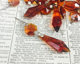 May include: A close-up of a group of amber glass crystal prisms with silver metal tops. The prisms are scattered on a page of a dictionary.