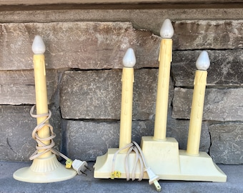 May include: Set of four vintage electric candle lamps with white bulbs and yellow candle-shaped bases. The lamps are plugged into a single cord and have a white base.