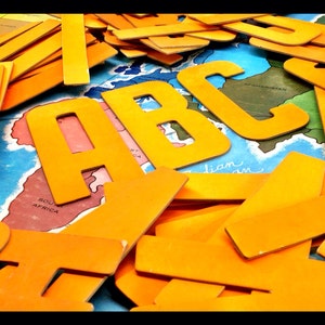 May include: A close-up of a pile of yellow cardboard letters that spell out "ABC". The letters are arranged on a map of the world with the text "Afghanistan" and "South Africa" visible.