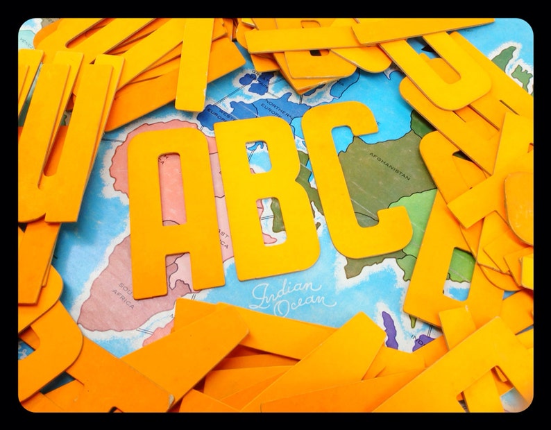 May include: Yellow plastic letters spelling out "ABC" on top of a world map. The letters are large and bold, and the map is colorful and detailed.