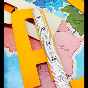 May include: A yellow letter 'F' made of cardboard, a ruler, and a world map with continents and countries labeled. The ruler is marked in inches and reads 'DURALL MADE IN USA'.