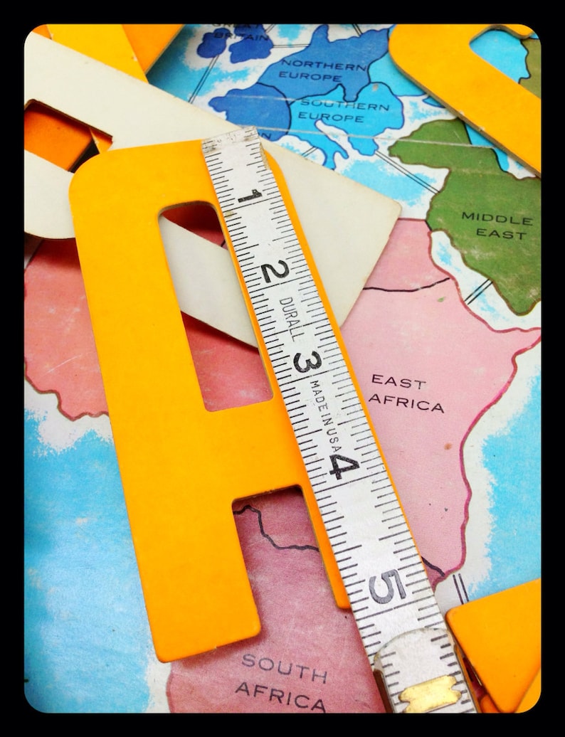 May include: A yellow letter 'F' made of cardboard, a ruler, and a world map with continents and countries labeled. The ruler is marked in inches and reads 'DURALL MADE IN USA'.
