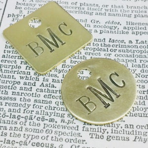 May include: Two brass keychains with the initials "BMC" engraved on them. One keychain is square and the other is round. Both keychains have a hole for attaching a key ring.