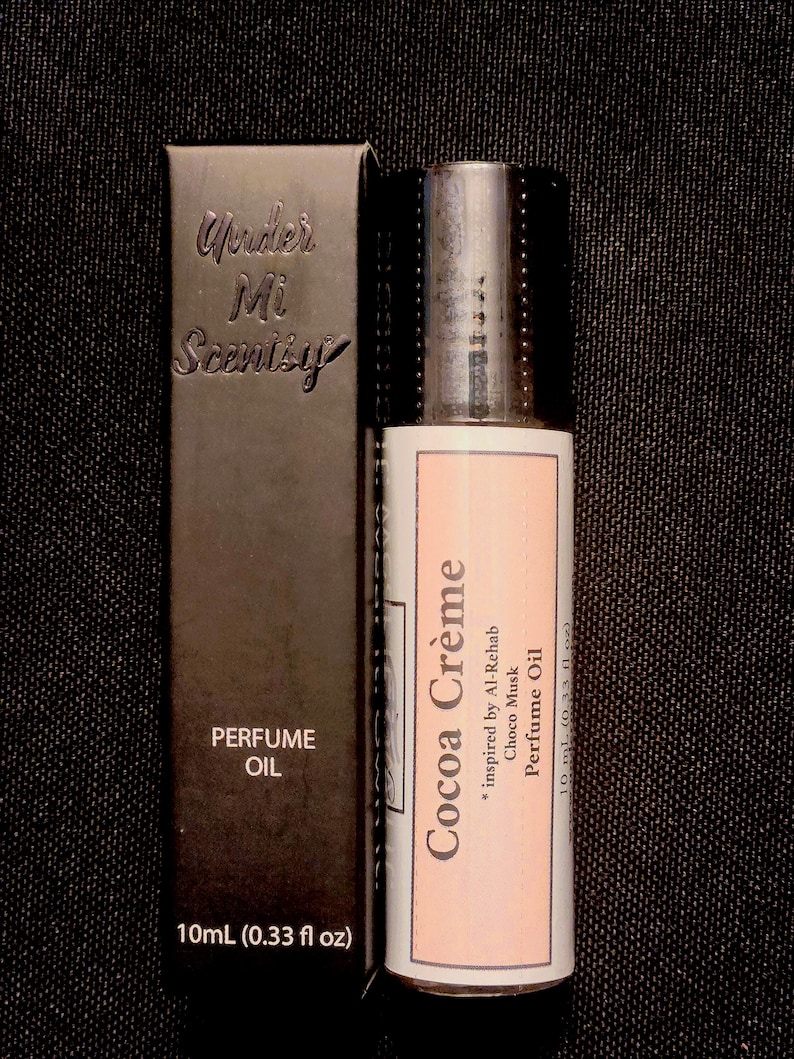 Puede incluir: Una caja rectangular negra de aceite de perfume etiquetada Under Mi Scentsy y 10 ml (0,33 fl oz) junto a una botella cil&iacute;ndrica de aceite de perfume con una etiqueta rosa claro que dice Cocoa Cr&egrave;me, inspirado en Al-Rehab Choco Musk, 10 ml.