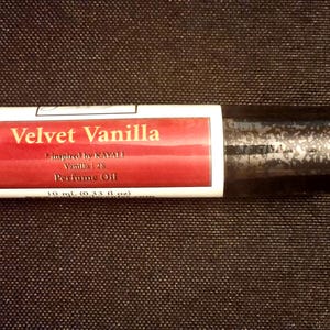 May include: A cylindrical perfume oil roller bottle with a white label featuring a red rectangular accent. The text reads Velvet Vanilla, inspired by KAYALI Vanilla | 28, Perfume Oil, and 10 ml (0.33 fl oz). The cap is black with a textured finish.