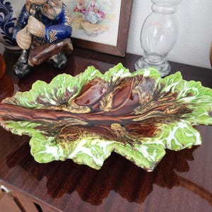 May include: A ceramic serving dish shaped like a large, ruffled leaf. The center features a deep, glossy brown glaze with textured, wood-like veins, while the outer edges are finished in a vibrant, variegated light green and white glaze.