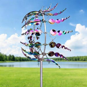 May include: A multi-colored metal wind spinner with a reflective, iridescent finish. The garden art features circular and leaf-shaped elements arranged on a central pole. The background includes a green lawn, lake, and blue sky.
