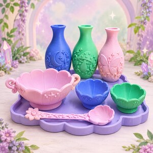 May include: A set of three vases in blue, green, and pink with embossed moon, mushroom, and butterfly designs. Includes a large pink bowl with handles, two smaller blue and green bowls, a pink spoon, and a purple tray with scalloped edges.