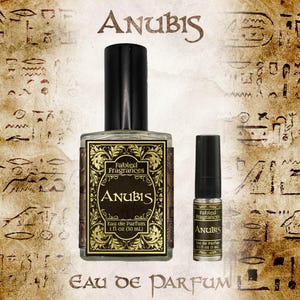 Peut inclure: Un flacon de parfum en verre transparent avec un bouchon noir et une étiquette rectangulaire aux bordures dorées ornées portant le texte Fabled Fragrances Anubis Eau de Parfum 30 ml, accompagné d'un échantillon assorti de 3 ml.