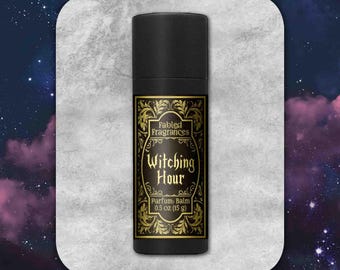 May include: A black cylindrical tube of Fabled Fragrances Witching Hour parfum balm. The label features gold ornate filigree borders and black text reading Fabled Fragrances, Witching Hour, Parfum Balm, and 0.5 oz (15 g) on a black background.