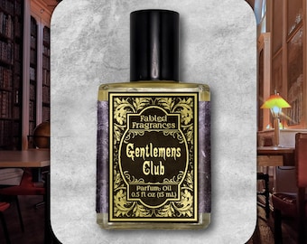 Può includere: Un flacone di olio profumato con tappo nero ed etichetta con la scritta "Fabled Fragrances Gentlemen's Club Parfum Oil 0.5 fl oz (15 ml)." L'etichetta presenta dettagli dorati ornati su sfondo scuro. Il flacone è rettangolare.