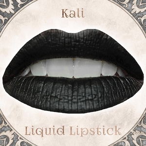 May include: A pair of lips coated in matte black liquid lipstick, showing a textured finish and white teeth. The word Kali is printed above the lips, and the words Liquid Lipstick are printed below, all set within a circular decorative frame.