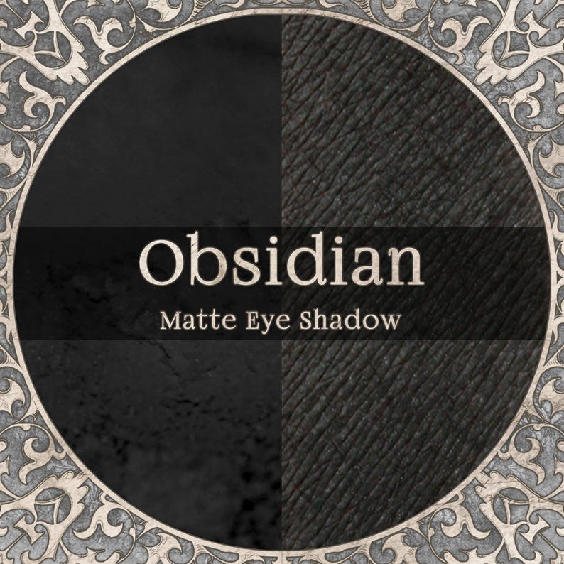 May include: A circular graphic featuring the text Obsidian Matte Eye Shadow in the center. The background is split into two black textures, one smooth and one grained, surrounded by an ornate, light-colored, decorative filigree border.