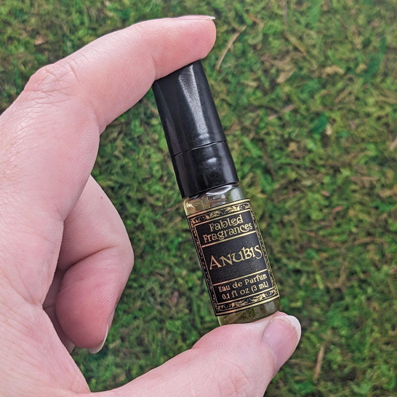 a hand holding a small black and gold bottle