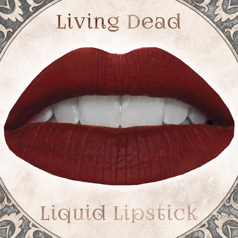 May include: A pair of lips coated in a deep, matte dark red liquid lipstick, showing white teeth. The image features the text Living Dead above the lips and Liquid Lipstick below, all framed within a circular border with ornate gray corner details.