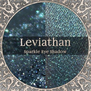 May include: A close-up of a round, dark teal eyeshadow compact with a decorative border. The eyeshadow is divided into four sections, each with a different texture and sparkle. The text "Leviathan Sparkle Eye Shadow" is displayed in the center.