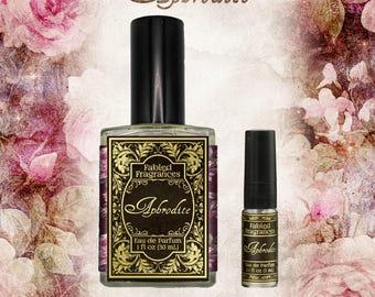 May include: A large and a small glass bottle of Fabled Fragrances Aphrodite Eau de Parfum. The large bottle contains 30 ml and the small bottle contains 3 ml. Both feature black caps and ornate gold and black labels with decorative borders.