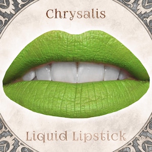 Könnte beinhalten: Ein Paar Lippen, die mit einem leuchtend matten, lindgrünen Flüssiglippenstift geschminkt sind. Das Wort Chrysalis ist in Braun über den Lippen aufgedruckt, und die Worte Liquid Lipstick stehen in Braun darunter, alles in einem runden Rahmen.