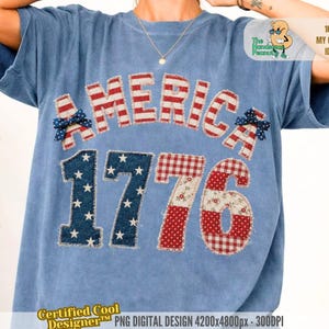 May include: A light blue t-shirt with the word "AMERICA" in red and white stripes and the numbers "1776" in a patchwork design. The number "1" is navy blue with white stars, and the "76" is red and white checkered and floral patterns.