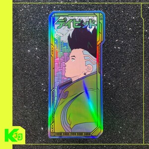 May include: Holographic sticker with a futuristic character design. The sticker has a green and blue iridescent finish, with Japanese text at the top and a cityscape in the background. The sticker is rectangular in shape, with a neon green border.