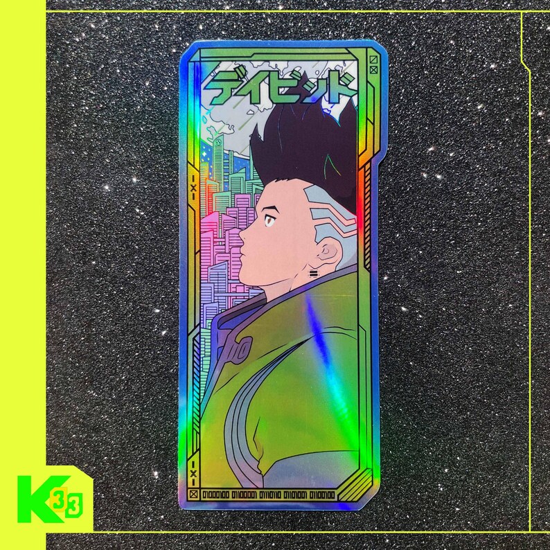 May include: Holographic sticker with a futuristic character design. The sticker has a green and blue iridescent finish, with Japanese text at the top and a cityscape in the background. The sticker is rectangular in shape, with a neon green border.
