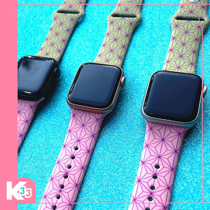 Op de afbeelding: Drie smartwatches met zwarte schermen en bandjes met patronen. De bandjes wisselen af tussen roze met paarse geometrische ontwerpen en olijfgroen met vergelijkbare patronen. De horloges hebben verschillende gekleurde behuizingen, waaronder zwart, goud en zilver.