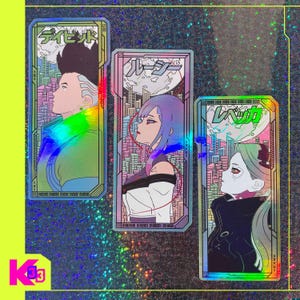 May include: Three holographic stickers with anime-style characters and Japanese text. Each sticker has a unique design with a cityscape background and vibrant colours. The stickers are rectangular with a neon green border and a holographic effect.
