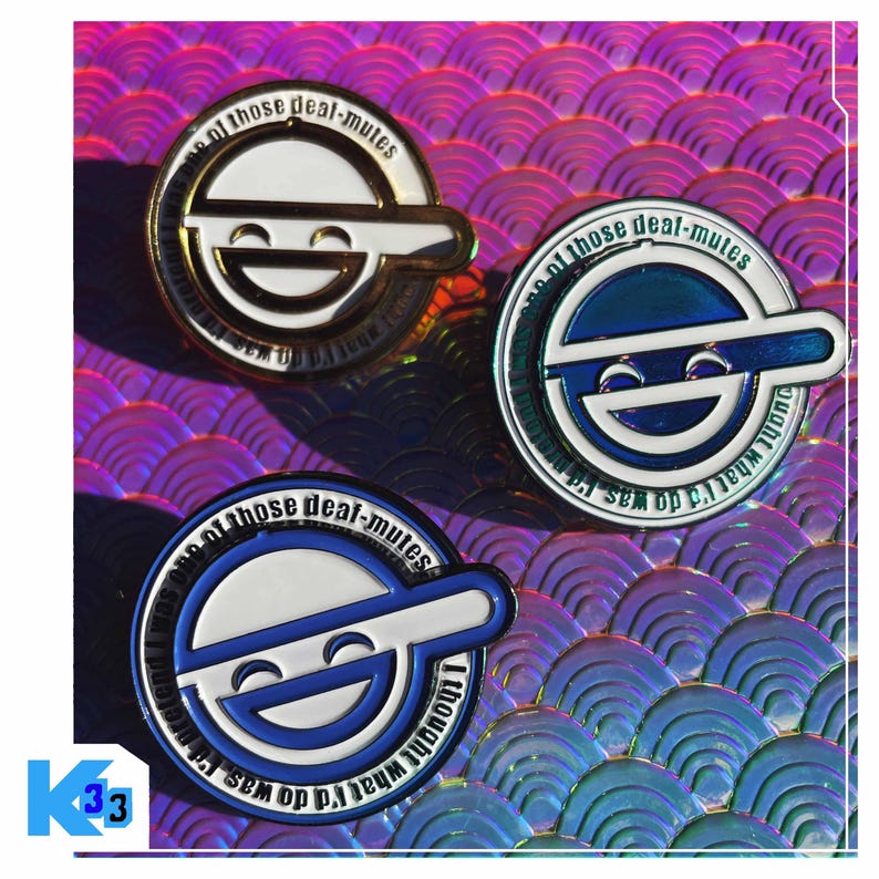 May include: Three metal pins with a smiling face design. The pins are in gold, blue, and silver, with the text "of those deal-mutes" and "I thought what I'd do was" around the edges. The background is a holographic, iridescent surface.