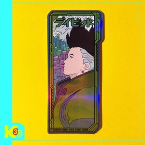 May include: A holographic sticker with a futuristic design, featuring a profile of a person with a unique hairstyle. The sticker has Japanese text at the top and a cityscape in the background, framed by a green and gold border. The background is yellow.
