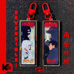 Könnte beinhalten: Zwei rechteckige Schlüsselanhänger mit roten Verschlüssen. Jeder Schlüsselanhänger zeigt eine andere Illustration im Anime-Stil mit japanischem Text. Eine Seite zeigt "REVERSIBLE!" in Rot. Die Schlüsselanhänger befinden sich in einer roten und schwarzen Umgebung.