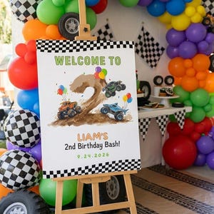 May include: A white rectangular sign on a wooden easel featuring a large brown number two, monster trucks, and colorful balloons. The text reads: WELCOME TO LIAM'S 2nd Birthday Bash! 9.24.2026. The sign has a black and white checkered border at the top and bottom.