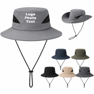 Op de afbeelding: Een grijze bucket hat met een brede rand, zwarte mesh zijpanelen en een verstelbaar zwart kinkoord. Op de voorkant van de hoed staat de witte tekst Logo Photo Text. Andere hoeden in marineblauw, olijfgroen, zwart, beige en donkergrijs zijn afgebeeld.