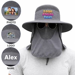 May include: A dark grey sun hat with a wide brim, mesh crown, and a detachable face flap covering the nose and mouth. The front of the hat features the text Logo Photo Text in yellow, pink, and blue. Includes circular insets showing a family photo, a fishing logo, and the name Alex.