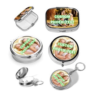 May include: A collection of silver-toned metal pill cases and keychains featuring custom photo and text prints. The items include rectangular and circular hinged containers with white plastic interiors, some with attached key rings and printed text.