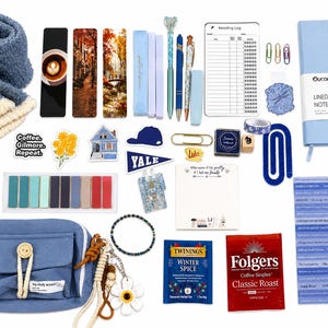 May include: A collection of stationery and lifestyle items including a blue fuzzy scarf, a light blue notebook, a blue zippered pouch, various bookmarks, pens, stickers, paper clips, a reading log, tea bags, coffee singles, and a sheet of inspirational quote stickers.