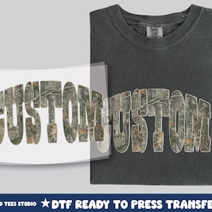 May include: A dark gray t-shirt with the word "CUSTOM" in a camouflage pattern. A DTF (Direct to Film) ready to press transfer of the same design is shown next to the shirt. The text "TWISTED TEES STUDIO" is at the bottom.