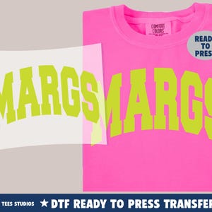 May include: A hot pink sweatshirt with the word "MARGS" in a lime green, arched font. A "READY TO PRESS" sticker is on the upper right. A DTF ready to press transfer is shown on the left.