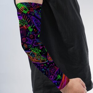 May include: A black arm sleeve featuring a vibrant neon-colored graphic print of various space-themed elements including flying saucers, stars, and abstract shapes in shades of green, blue, purple, pink, and orange against a dark background.