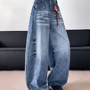 Three-quarter angle view of the wide-leg blue denim pants, highlighting the loose fit, faded wash, and vertical seam details.