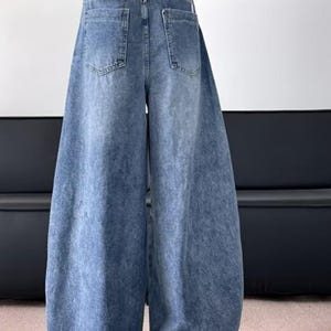 Rear view of the loose-fitting blue denim pants showing the two back pockets and the wide flared silhouette.