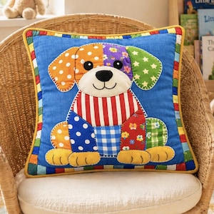 May include: A square throw pillow with a blue background featuring a colorful patchwork dog design. The dog has ears with orange polka dots and green stars, a red and white striped chest, and a blue and white checkered belly with floral accents.