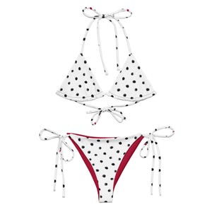 May include: A white bikini set with black polka dots. The top is a halter style with tie closures, and the bottoms are a classic string style with a red interior. The swimwear is designed for a comfortable and stylish beach or poolside look.