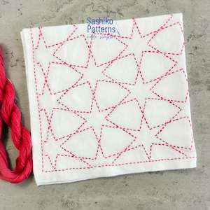 Peut inclure: Carré de tissu blanc avec un motif d'étoiles rouges cousu en pointillé. Le texte "Sashiko Patterns made simpler" est visible. Un fil rouge est visible dans le coin inférieur gauche.