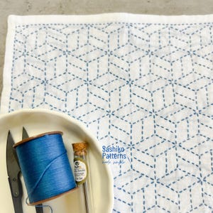 Pode incluir: Tecido branco com um padrão geométrico azul costurado. Uma tigela contém linha azul, tesouras e agulhas. O texto "Sashiko Patterns made simple" é visível.